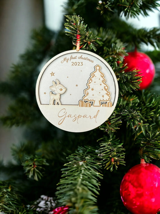 Une decoration de Noel en bois suspendue à un sapin, gravée avec le texte "My First Christmas" en haut et le prénom "Gaspard" en bas. Le design inclut un petit renne et un sapin décoré, entourés de cadeaux et d'étoiles. La décoration est suspendue à un ruban rouge, ajoutant une touche festive et personnalisée pour célébrer le premier Noel de l'enfant.